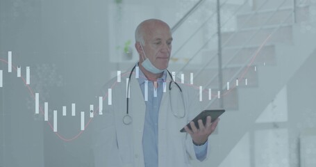 Reviewing data male doctor holding tablet in medical lobby, with stethoscope surgical mask charts