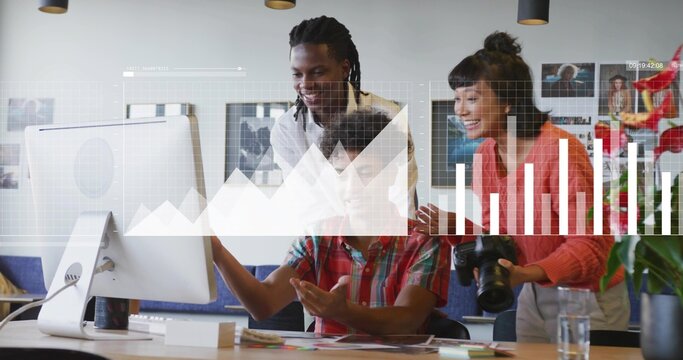 Three colleagues collaborating around computer monitor in office, with DSLR camera and notebooks