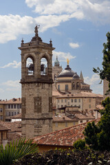 Vertical composition captures Bergamo layered skyline where historic towers align in depth, showing cathedral bells, domes, and spires rising above terracotta rooftops
