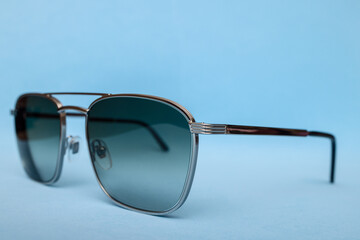 Minimalist product photo of modern sunglasses with metallic frame and smoky gradient lenses, placed against smooth pastel blue background creating clean elegant mood