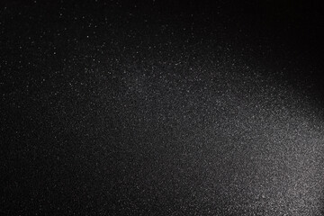 Black glitter background with fine micro texture illuminated from lower right corner, shimmering particles create elegant gradient effect with cosmic depth