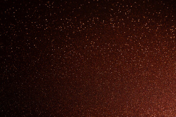 Red brown glitter background with shadowed edges and bright spot in lower left, sparkling grains spread outward creating radiant shimmering abstract composition