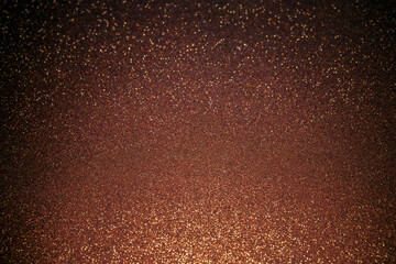 Brown glitter surface illuminated from bottom, glowing sparkles rise into darker tones creating...