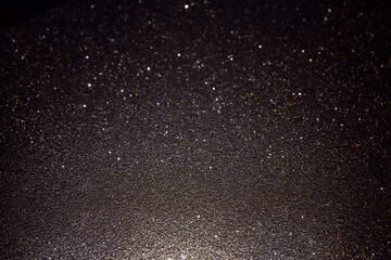 Obraz premium Dark glitter texture illuminated from below, highlighting surface detail and rare sparkles creating abstract background with subtle luminous depth