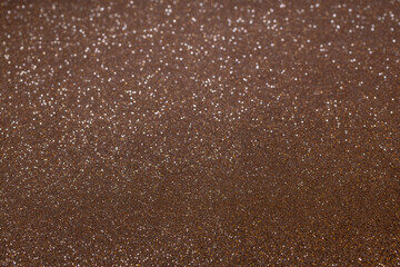 Glittering brown texture glowing under light, forming abstract scene with clear granular details below and smooth blurred sparkles toward top frame