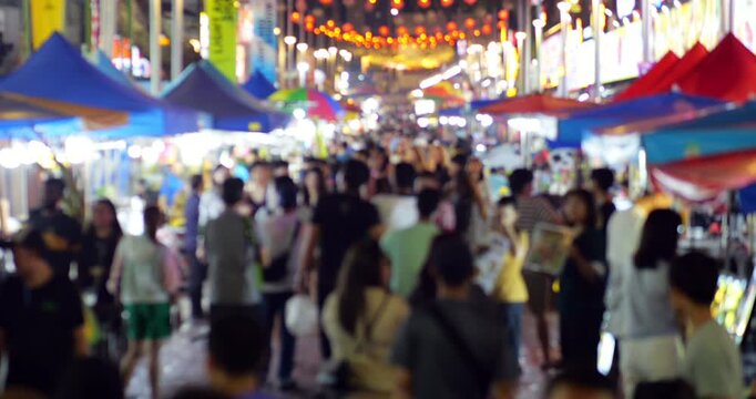 Blurred view on crowded night market street. Many people walking through bustling Asian food street at night in Kuala Lumpur, with colorful stalls and festive lights creating vibrant atmosphere.