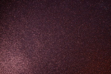 Burgundy glitter texture glowing with warm sparkles, macro surface evenly focused while soft light from lower left creates radiant abstract gradient
