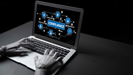 A robotic hand engages with a laptop showcasing compliance-related concepts, emphasizing the...