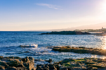 black rock sea beach during sunrise or sunset with golden sand, mild surf, blue calm water and...