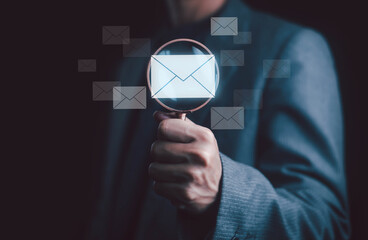 Businessman holding magnifying glass focusing on email icon, representing email marketing analysis, digital communication, data research, and online business strategy concept.