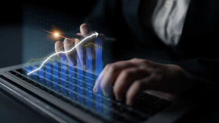 A close-up view of hands typing on a laptop while interacting with financial graphs and data,...