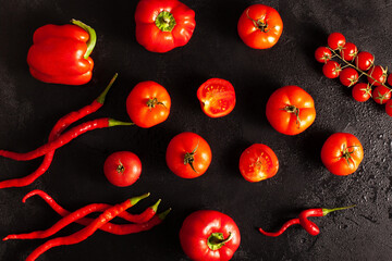 Mix of ripe red tomatoes, cherry tomatoes, bell peppers, and chili peppers on a dark textured surface. Fresh organic vegetables perfect for cooking, recipes, and healthy eating concepts.