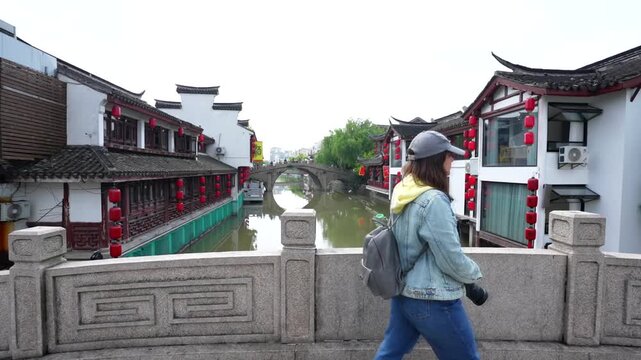 Slow motion of a photographer crossing a small Qibao canal bridge with red lanterned houses visible behind her. Shanghai, China