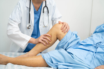 Doctor checking Asian elderly woman patient with scar knee replacement surgery in hospital.