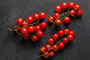 Ripe cherry tomatoes on stems arranged on dark background. Natural organic vegetables ideal for vegan diet, healthy lifestyle, and farm produce design.
