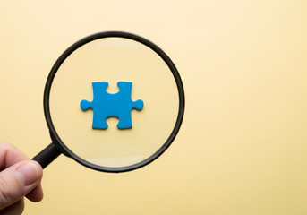 Magnifying glass focusing on blue puzzle on light yellow surface, concept of discovery, teamwork, problem solving, analysis, creative idea
