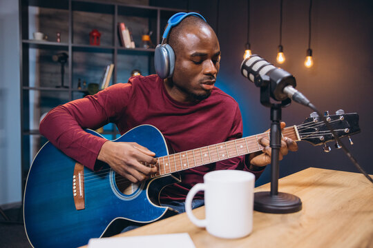 Young African American man playing acoustic guitar and recording music or interview for his podcast in a home studio