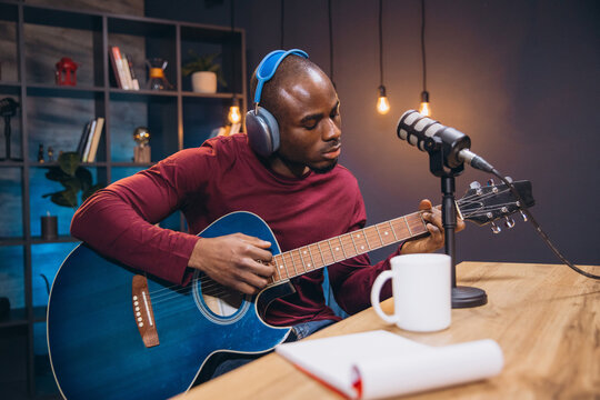 Young African American man playing acoustic guitar and recording music for podcast in home studio