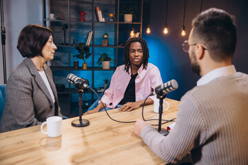 Three podcasters, two hosts and a guest, are recording a new episode in a professional studio, engaging in a discussion