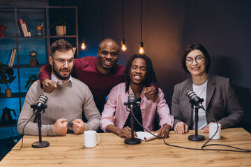 Four podcasters sitting at a table with microphones, recording a new episode in a professional studio
