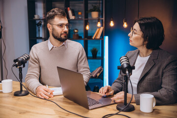 Content creators recording their podcast using microphones and laptop in a studio with blue light and bookshelf