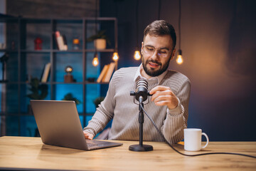 Podcaster setting up microphone, wearing headphones near professional audio gear inside compact home recording workspace