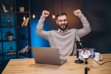 Successful podcaster cheering, arms raised during live recording session