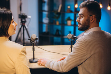 Professional podcasters recording audio content, discussing topics with microphones in soundproof studio setting