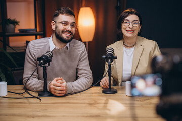 Two podcasters smiling and engaging while recording an exciting new episode in a modern studio filled with professional equipment