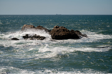 Waves crashing against rocky coast under bright sunlight by the open sea