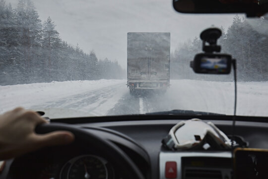 View from the eyes of the driver, from the windshield of the car on a winter road during a snowfall.Dangerous driving, snow is flying from the truck