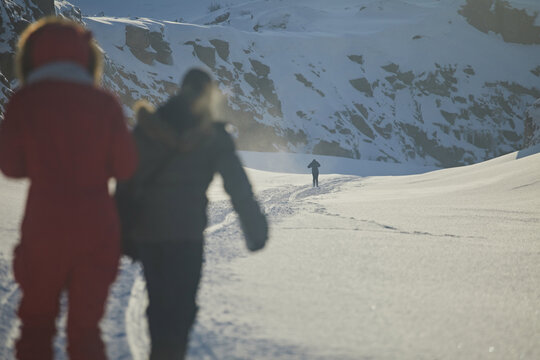 Two silhouettes of a girl walk along a snowy rut in the mountains in winter against the backdrop of a lonely man in a gorge