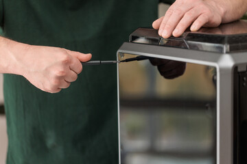 Man using screwdriver while assembling 3D printer, concept of maintenance, repair and technology setup.