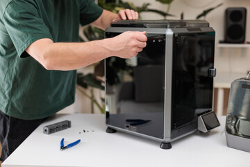 Man using screwdriver while assembling 3D printer, concept of maintenance, repair and technology setup.