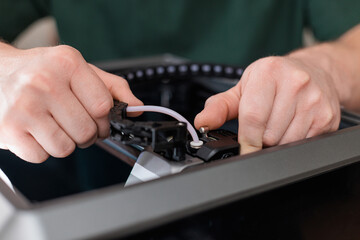 Hands cutting plastic tube with pliers during 3D printer maintenance, concept of precision and manual work.