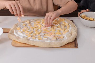 Children putting cheese on pizza dough, concept of home cooking and creative family time.