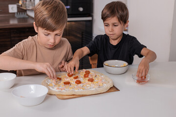 Two kids boys preparing pizza dough at home, concept of family cooking, learning and creativity.