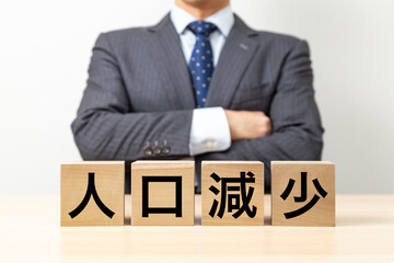 「人口減少」と書かれたブロックと腕組みをするビジネスマン