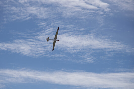 A white glider soars high in a blue sky adorned with wispy clouds.
