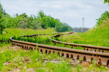 Curved railway tracks passing through green nature towards industrial city horizon. Railway tracks bend through lush greenery toward city skyline, symbolizing travel, transition, connection between