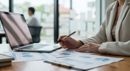 Woman works with laptop and documents in office setting.