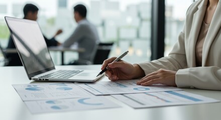 Businesswoman works with documents and laptop in office meeting with colleagues.