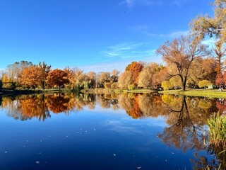 Fantastic vivid and colorful autumn trees reflection on the pure blue lake water, clear blue sky, beautiful golden fall