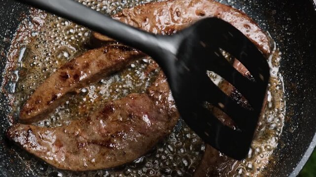 Top view of a kitchen spatula moving pieces of frying liver across the pan in boiling fat. Cooking beef liver according to the recipe. Preparing meat products from an eco farm.