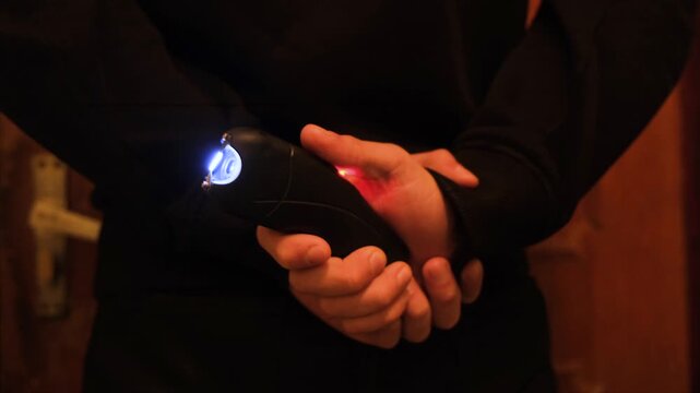 A man holds a stun gun behind his back, pressing the button and triggering an electric discharge. A personal defense tool against offenders and dangerous stray animals. Self defense and protection.
