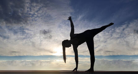 Silhouette of beautiful woman practicing yoga asana on the beach with sunrise on twilight blue vibrant sky and calm sea in background. Half moon pose Stretching June 21 Yoga Day ardha chandrasana pose