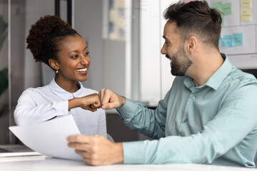 Obraz premium Excited multiracial diverse project partners reviewing papers share fist bump