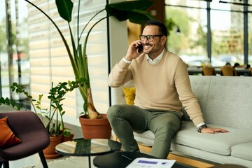 Smiling Man On The Phone In A Modern Office Lobby With Green Plants And Comfortable Sofa