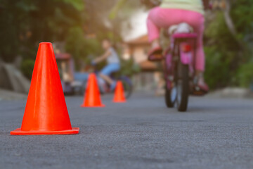 Focus to orange traffic cones on street with blurry group of children learn to riding bicycle in the evening after back from school. Background for outdoors activity or recreation concept.