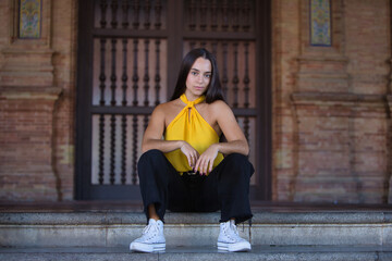 Young woman, brunette, Latina, wearing a yellow shirt, black jeans, and white sneakers, with a...